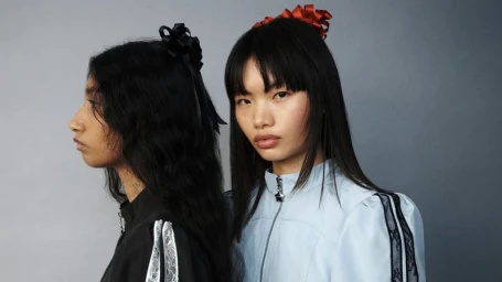 Two female models posing in profile and front view against a neutral grey studio backdrop for Sandy Liang Spring/Summer 2025 campaign.