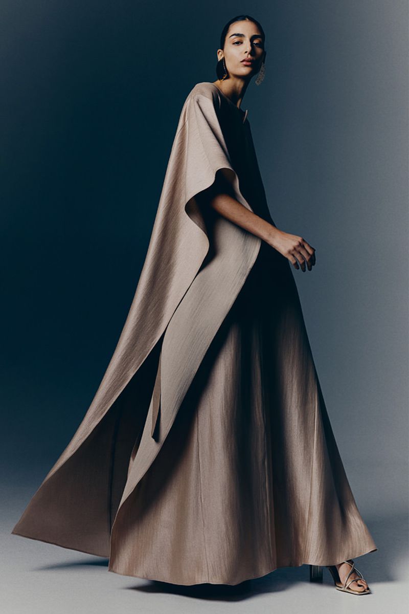 Woman in flowing beige gown, studio lighting. Elegant fashion shot featuring a sophisticated dress design and a graceful pose.