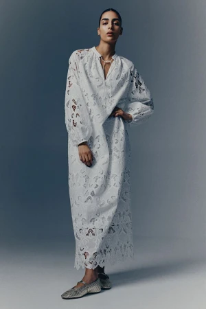 Model Nora Attal in a long white lace dress and metallic flats against a grey studio backdrop