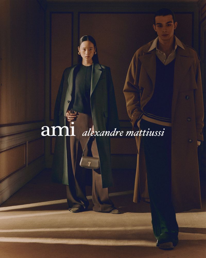 Two fashion models in an indoor environment, wearing coats and pants. The models are next to text overlay of 'ami alexandre mattiussi'.