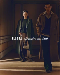 Two models standing in a softly lit interior hallway wearing tailored coats, photographed by Daniel Archer for Ami.