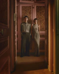 Two models standing in a narrow hallway with patterned pink paneling doors for AMI S/S 25