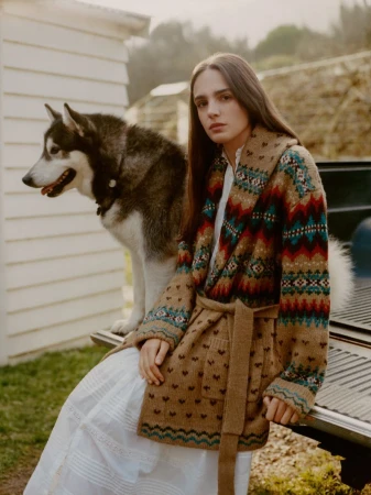 Young woman in patterned cardigan poses with a husky dog near the back of a pickup truck in an outdoor, rural setting.