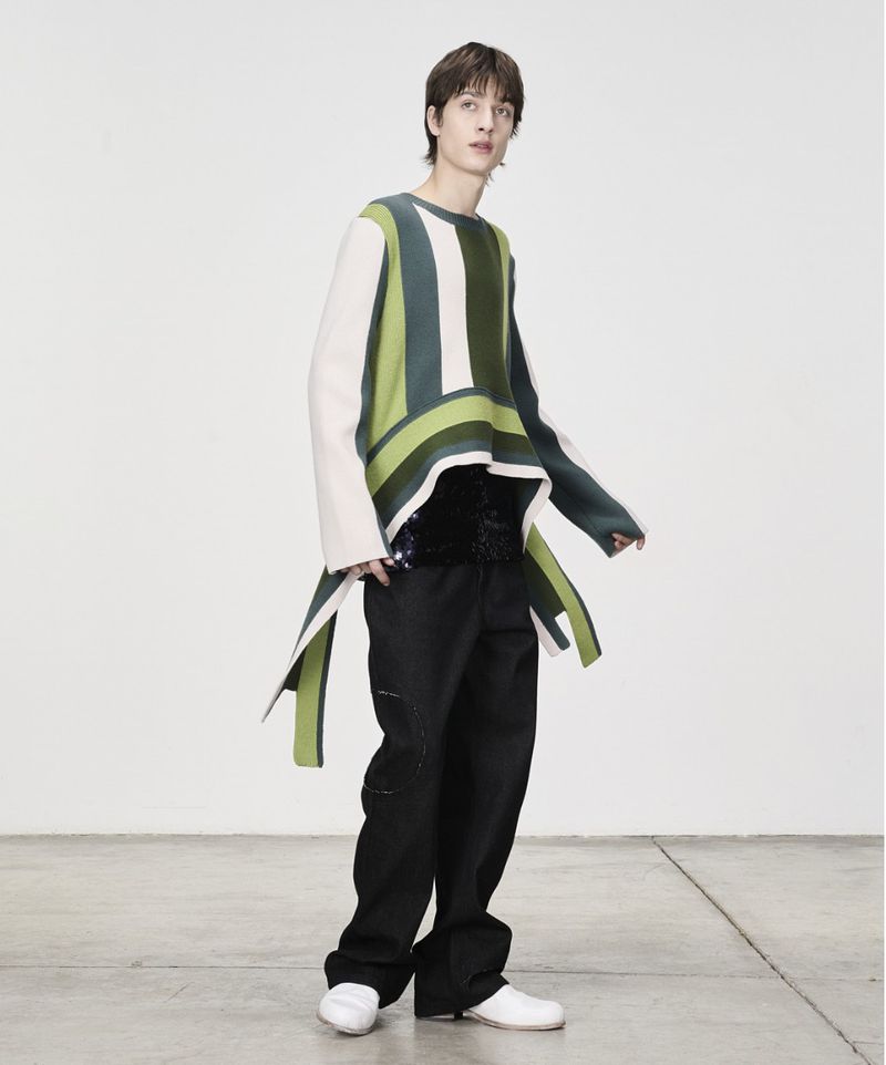 Model wearing a striped green sweater and black trousers against a neutral white background