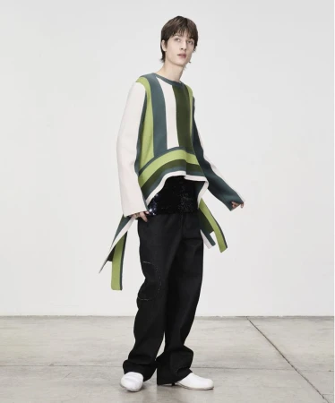 Model wearing a striped green sweater and black trousers against a neutral white background