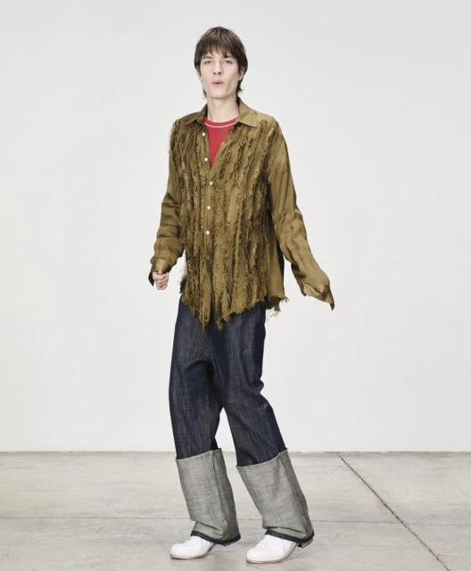 Full-shot studio portrait of a fair-skinned young adult wearing an open button-down shirt, jeans, and white shoes in a white studio.