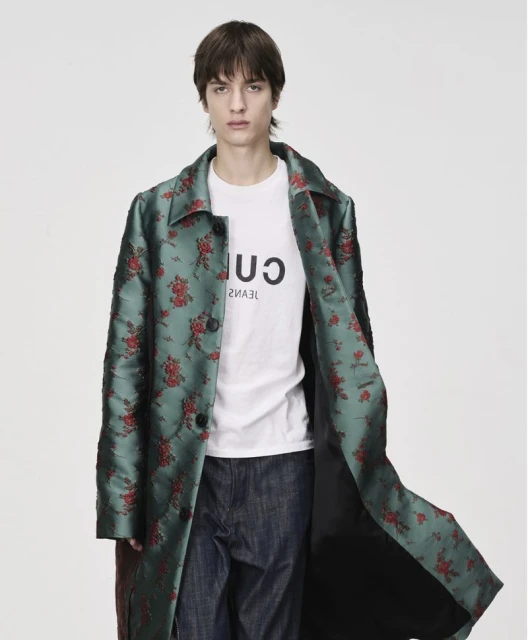Man wearing a floral print trench coat and jeans against a white backdrop in a studio fashion shoot.