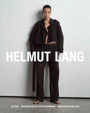 Model wearing a black cropped trench coat and matching trousers standing against a pale grey studio wall
