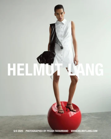 Model wearing white sleeveless shirt dress standing on a red sphere against a plain background