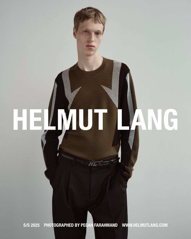 Model in brown patterned sweater and black trousers posing against a grey seamless studio backdrop for Helmut Lang