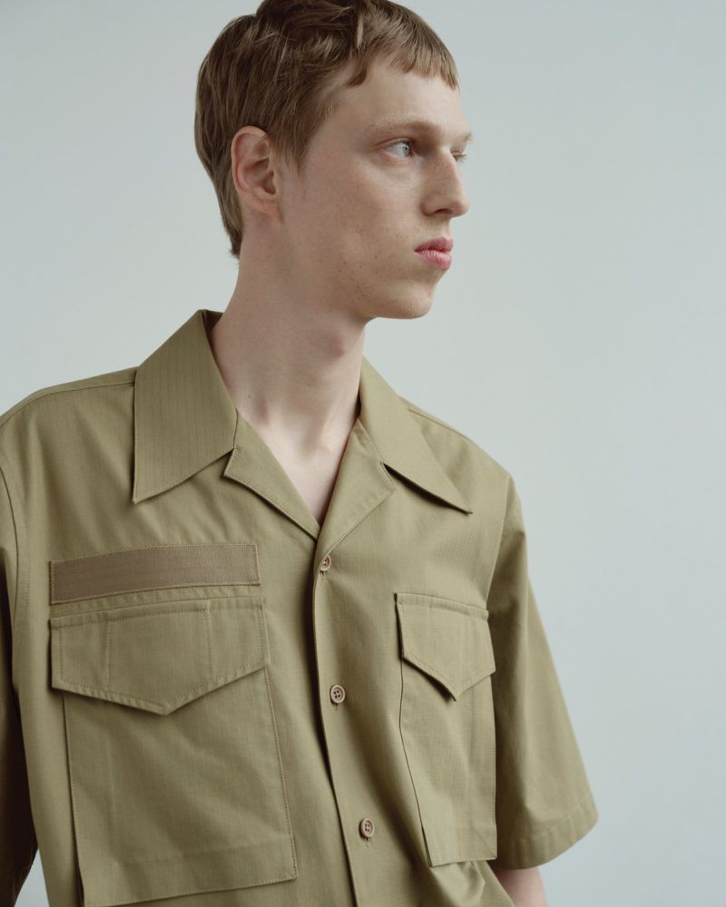 Portrait of an adult male with short, light brown hair wearing a short-sleeve, tan collared shirt and looking off camera against a neutral backdrop.