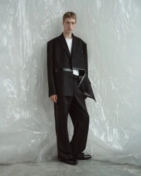 Model in a black suit with a white t-shirt standing against a wrinkled plastic textured background