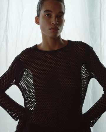 Model wearing a black mesh top posing against a white translucent curtain backdrop for Helmut Lang