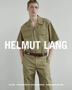 Model wearing an olive green short-sleeve utility shirt and matching trousers against a pale grey seamless background.