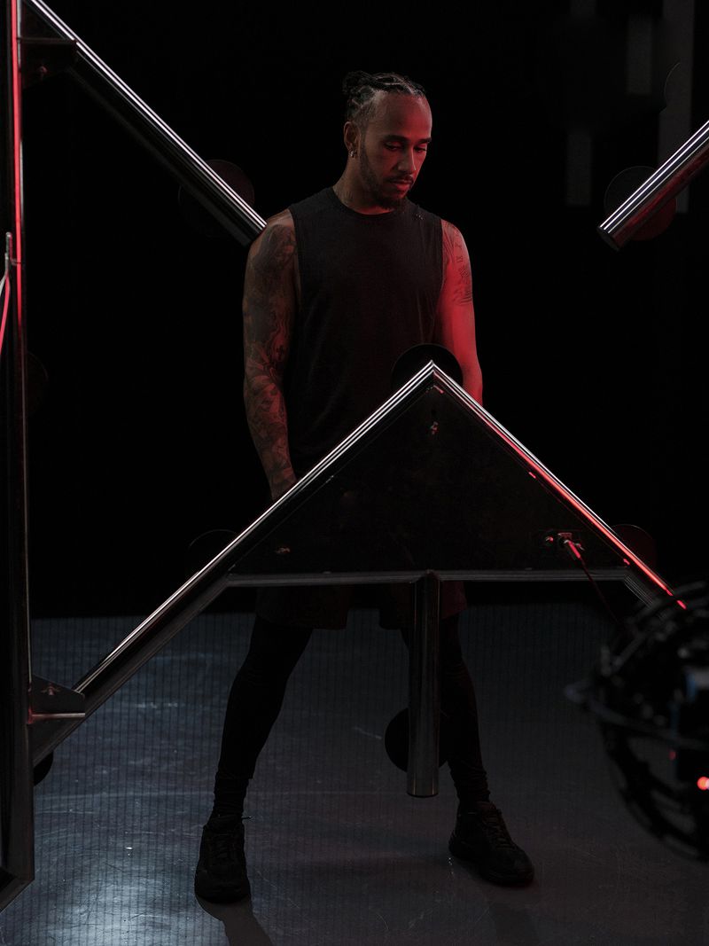 Portrait of adult male in a dark tank top standing under and behind metal square light fixtures with red light in an indoor environment.