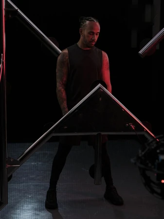 Portrait of adult male in a dark tank top standing under and behind metal square light fixtures with red light in an indoor environment.