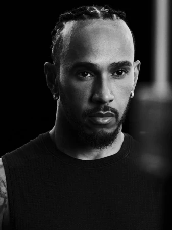 Monochromatic portrait of a Black adult male with hair in braids, wearing a dark tank top, and accessorized with diamond stud earrings.