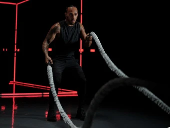 Lewis Hamilton working out with heavy battle ropes in a dark studio lit by geometric red neon lines