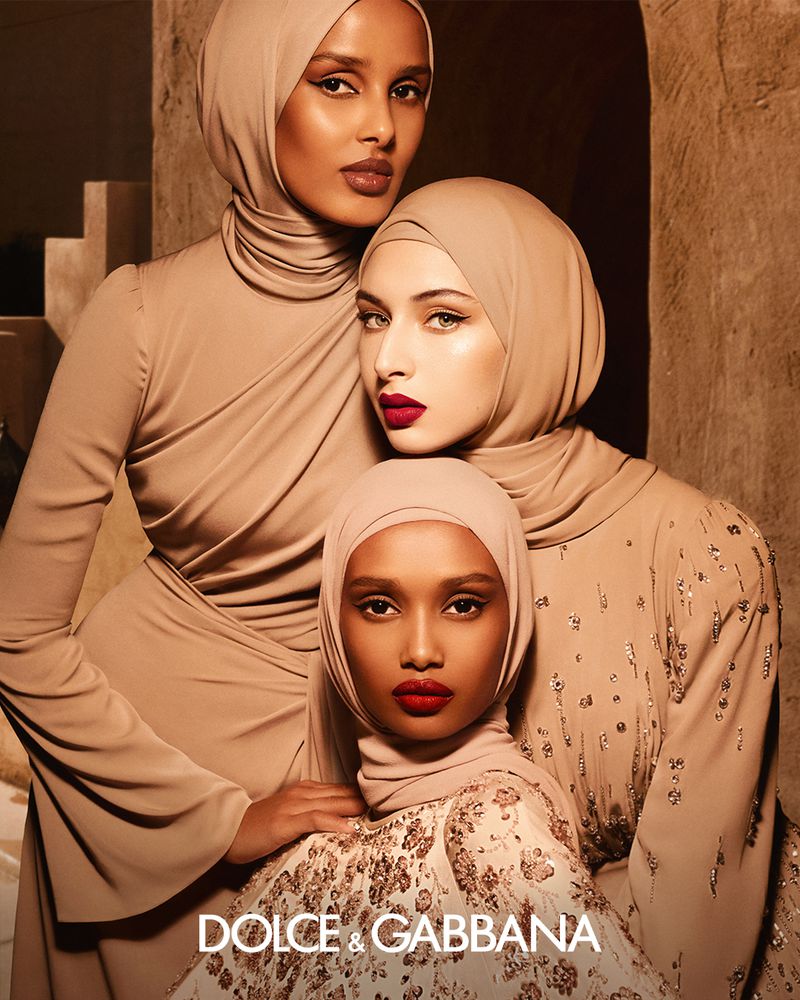 Three female models in matching beige hijabs and earth-toned garments posing together for Dolce and Gabbana Beauty.