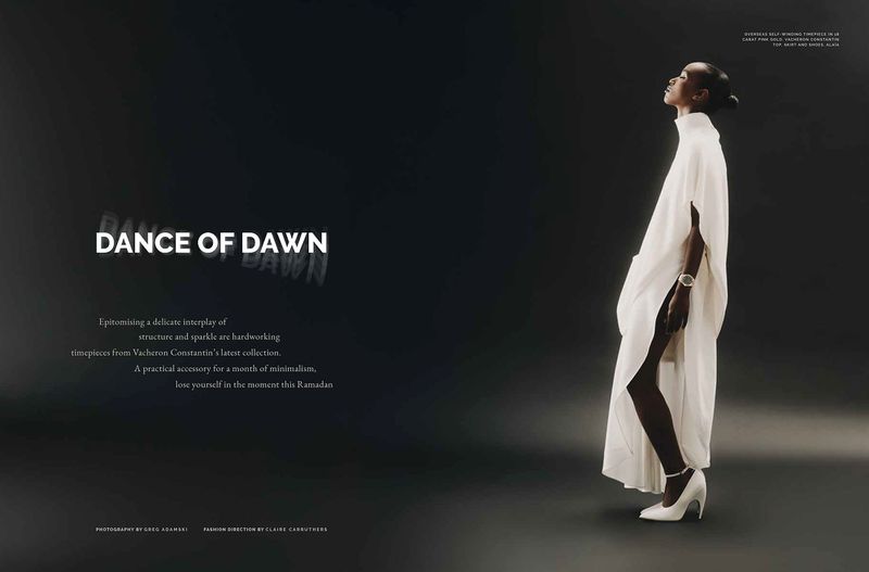 Elegant studio shot of an African-descent woman in a white kaftan and heels, accessorized with a wristwatch against a dark backdrop.