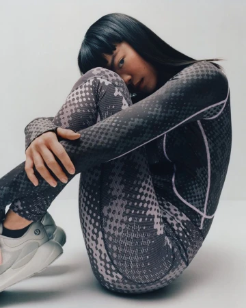 Woman in patterned athletic wear sits in studio. She is Asian, with black hair and white running shoes. The image features studio lighting.