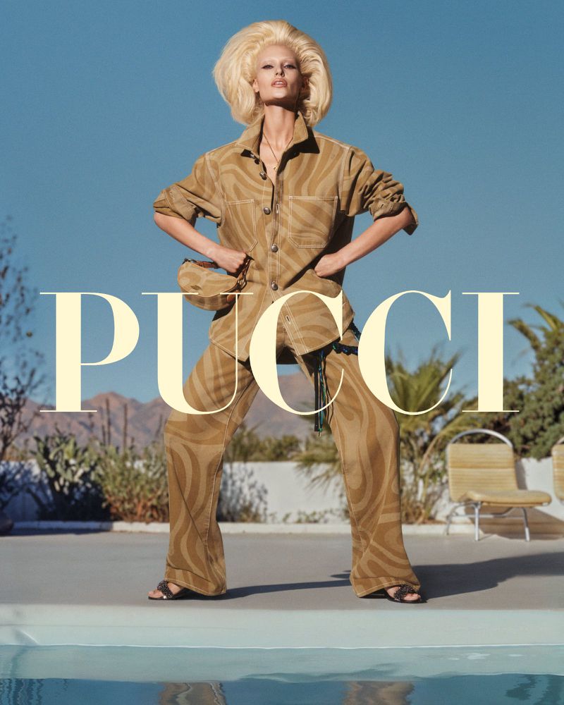A woman in a brown patterned pantsuit poses in front of a pool and mountain landscape, accented by the large PUCCI logo overlay.