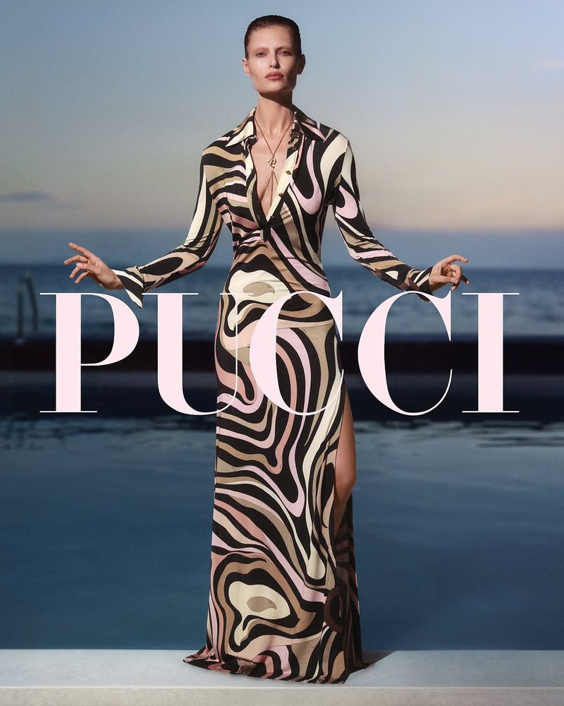 Elegant adult woman in a patterned dress strikes a pose in front of a pool at sunset. The brand name PUCCI is in foreground.