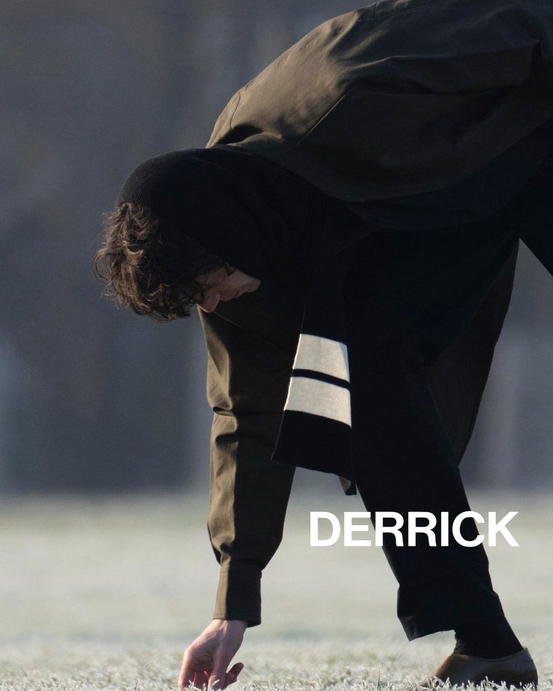 Young man in a dark coat bends over outdoors on a cold, frosty day with the name DERRICK in large, sans-serif text in the foreground.