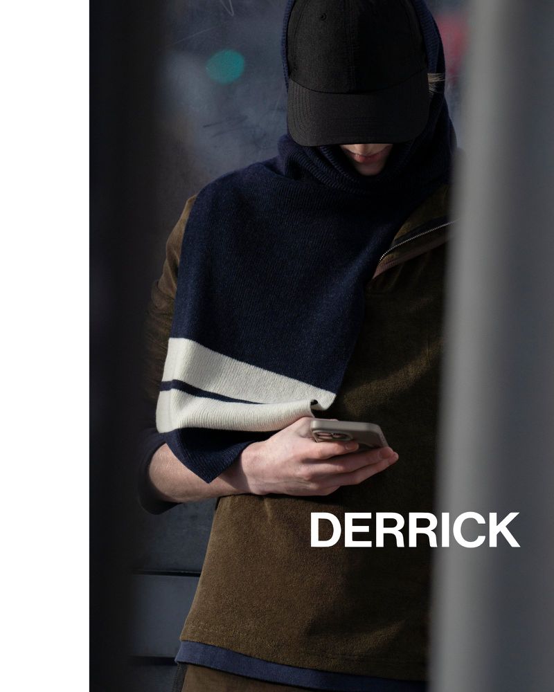 A person in a dark cap and striped scarf looks at a smartphone in an urban setting, creating a fashion-forward and modern aesthetic.