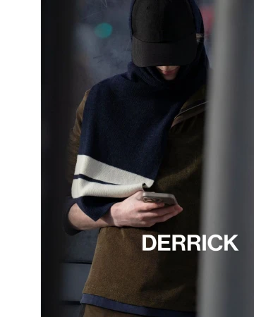 A person in a dark cap and striped scarf looks at a smartphone in an urban setting, creating a fashion-forward and modern aesthetic.