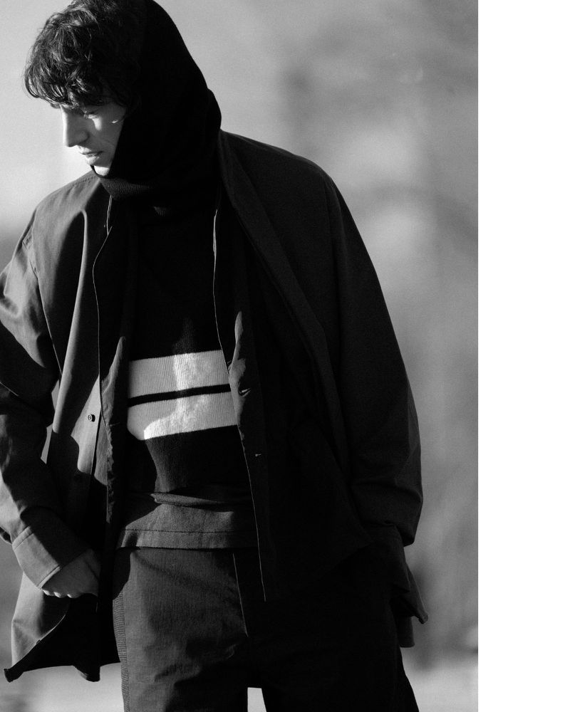 Monochrome portrait of a male model wearing a dark hooded sweater and jacket for Derrick Fall/Winter 25.