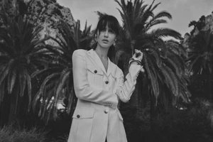 Monochrome fashion portrait of a female model wearing a white utility jacket outdoors against palm trees.