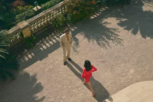 High-angle view of two models outdoors on a gravel terrace with a stone balustrade for the Tagliatore SS 2025 campaign.