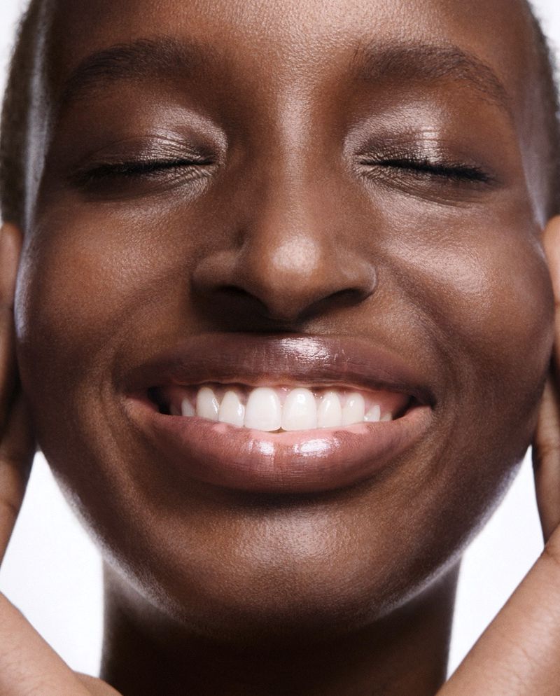 Close-up shot of a dark-skinned woman with her eyes closed and a happy expression, showcasing her teeth and skin texture.