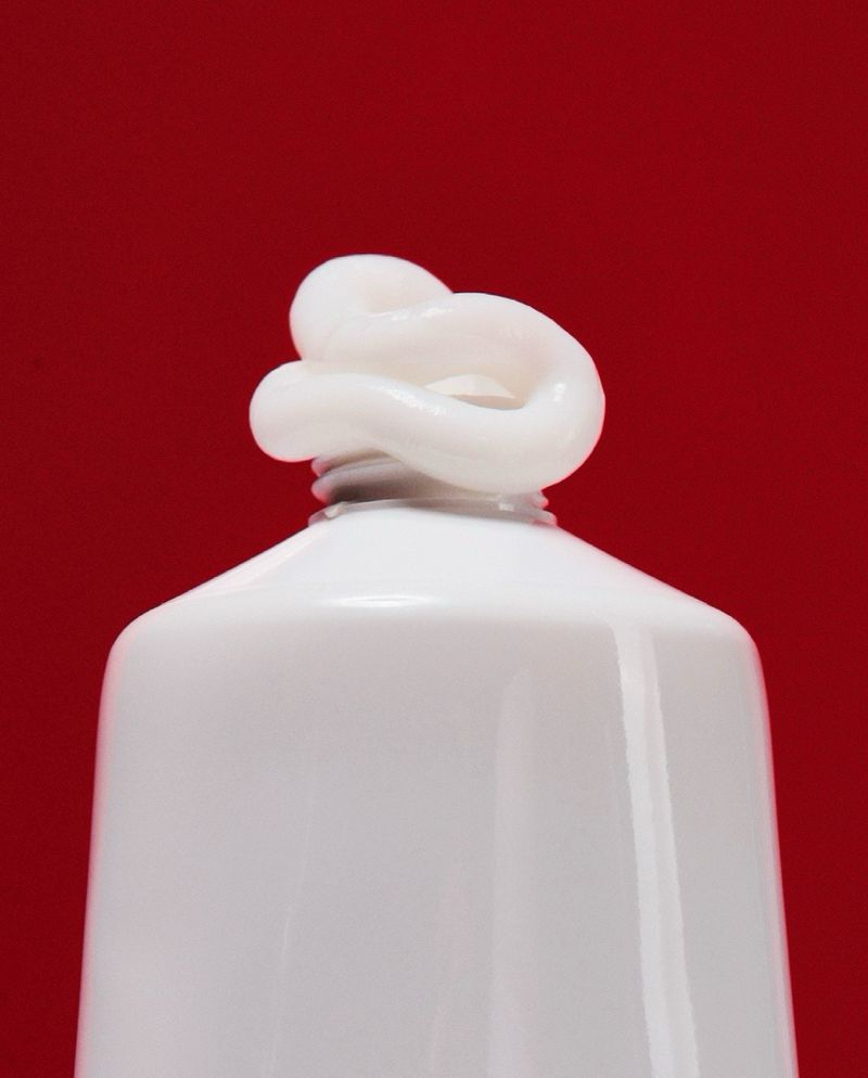 Close-up of white cream coming out of a white tube against a solid red background, suitable for beauty or healthcare themes.