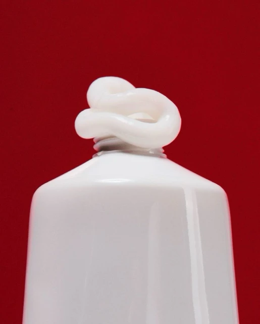 Close-up of white cream coming out of a white tube against a solid red background, suitable for beauty or healthcare themes.