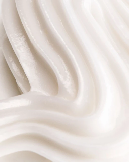Close-up of thick, glossy, smooth cream or lotion with curved ridges in a swirling pattern, creating an abstract, clean texture.