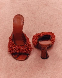 Pair of red beaded mules with patterned soles resting on a textured pink background