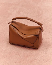 Tan leather shoulder bag resting on a textured pink surface for a Vogue.com editorial project