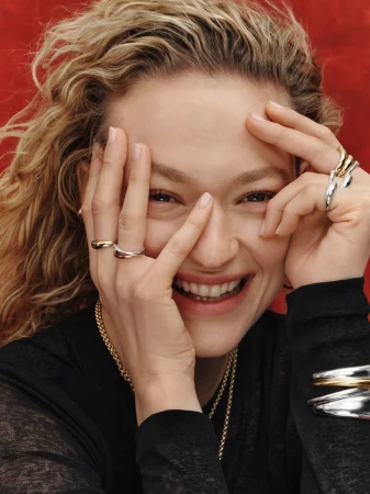 Close-up portrait of a smiling woman wearing multiple rings and bracelets against a textured red backdrop.