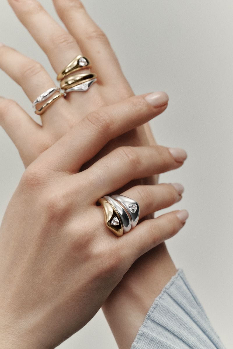Close-up of a fair-skinned adult female hand displaying gold and silver rings on a neutral background. Jewelry fashion shoot.