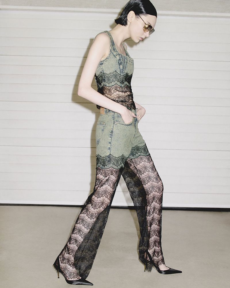 Fashionable woman in jeans and lace walking confidently against a neutral garage backdrop, showcasing unique style and modern elegance.