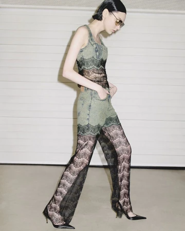 Fashionable woman in jeans and lace walking confidently against a neutral garage backdrop, showcasing unique style and modern elegance.