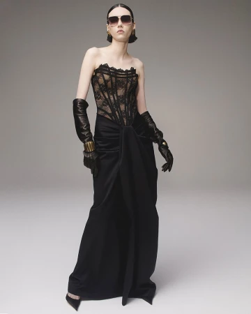 Model wearing a black strapless lace corset gown and long leather gloves against a neutral studio background.