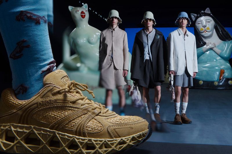 Tan Dior sneaker paired with patterned blue socks takes center stage in a runway presentation featuring models and sculptural cats.