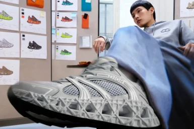 Model seated in a grey hoodie with a massive sneaker foreground for Dior Men Summer 2025 campaign