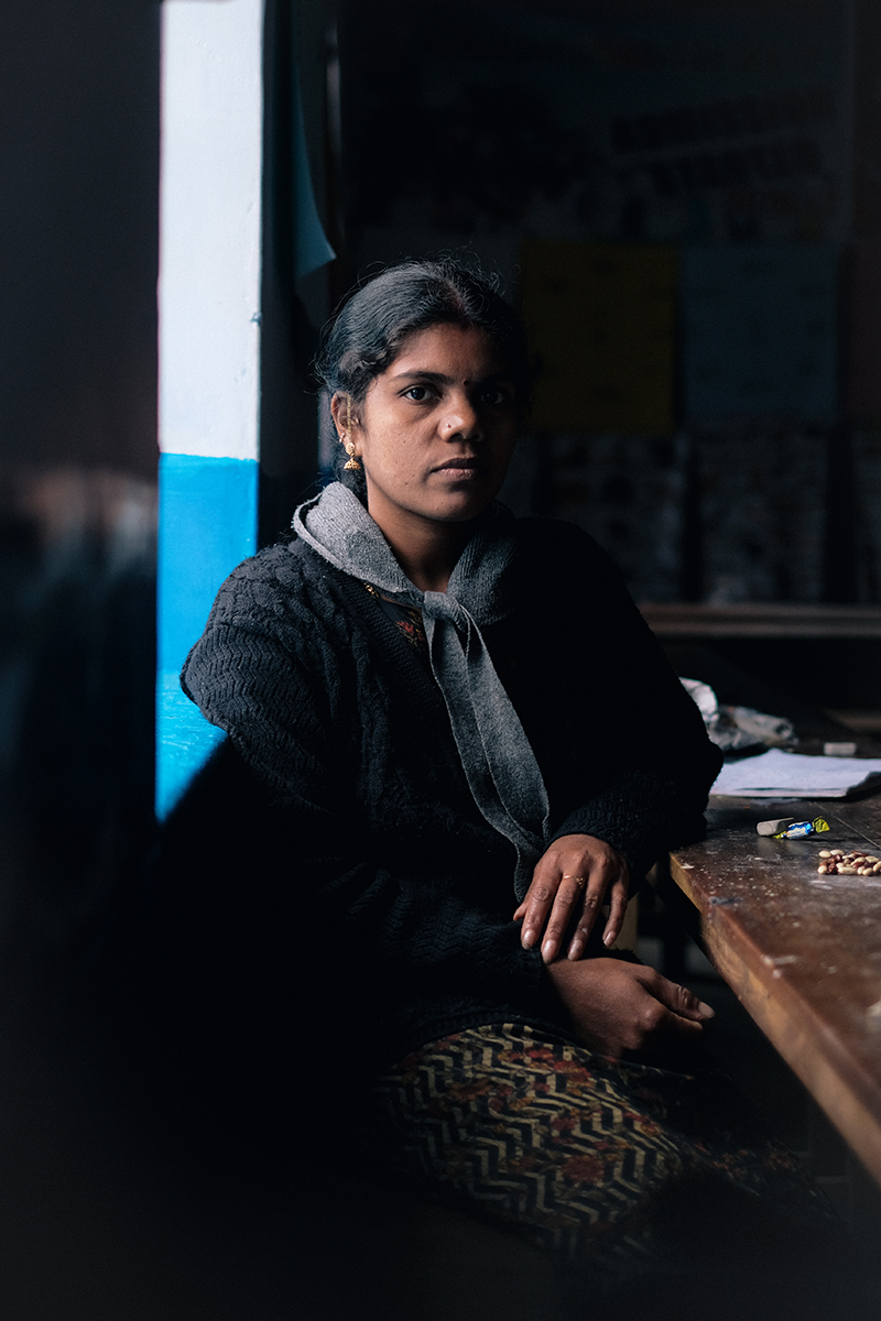 Portrait of a South Asian adult female with a serious expression sitting indoors near a table and window with natural lighting.