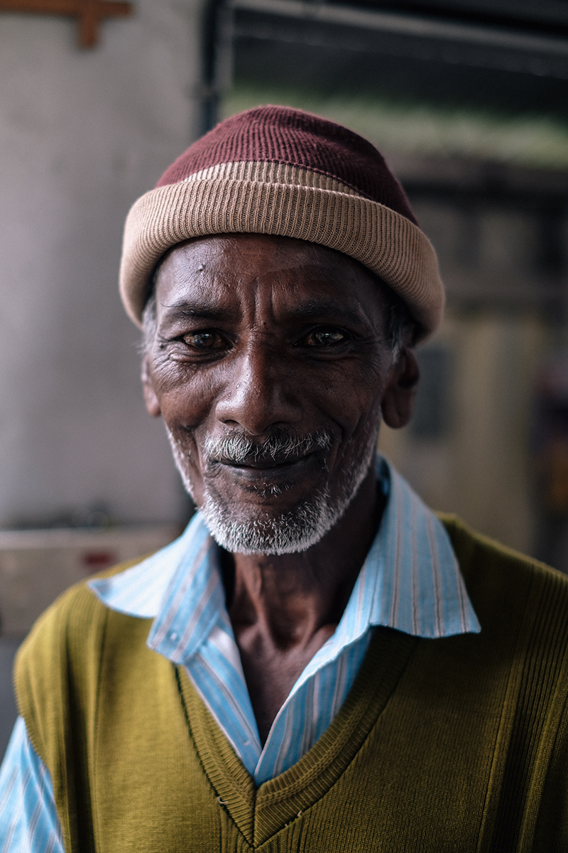 Portrait of an elderly man with a grey beard wearing a striped shirt and a ribbed beanie hat