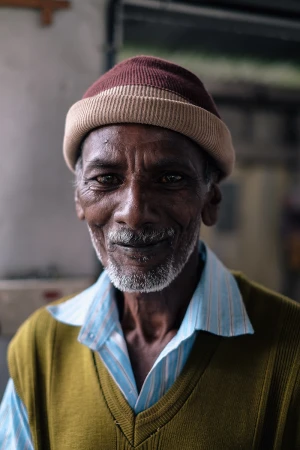 Portrait of an elderly man with a grey beard wearing a striped shirt and a ribbed beanie hat