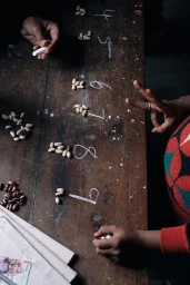 Overhead view of a person using chalk and beans to count on a dark wooden table in Ti Origin